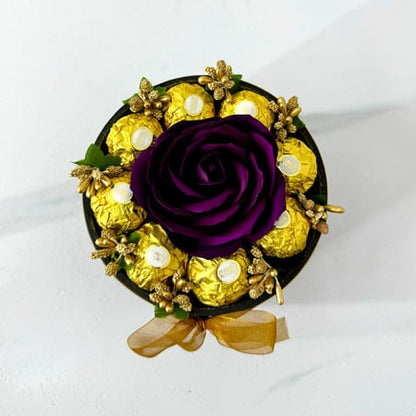 Blumenarrangement mit einer Seifenrose, goldenen Staubblättern und 8 Ferrero Rocher, schwarzer Samtschachtel, violett-burgunderfarben